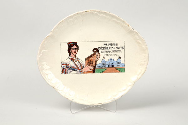 Dekoratīvs šķīvis, veltīts V Vispārējiem latviešu Dziesmu svētkiem Rīgā. 1910. gads. Izgatavots Vācijā keramikas fabrikā Villeroy&Boch, apgleznots Rīgā, J. Jaksch&Co fajansa un porcelāna apgleznošanas darbnīcā