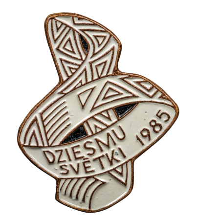 Nozīmīte - izrakstīta josta savīta nošu atslēgas formā, balta emalja ar zelta krāsas ornamentu un uzrakstu: "Dziesmu svetki 1985"